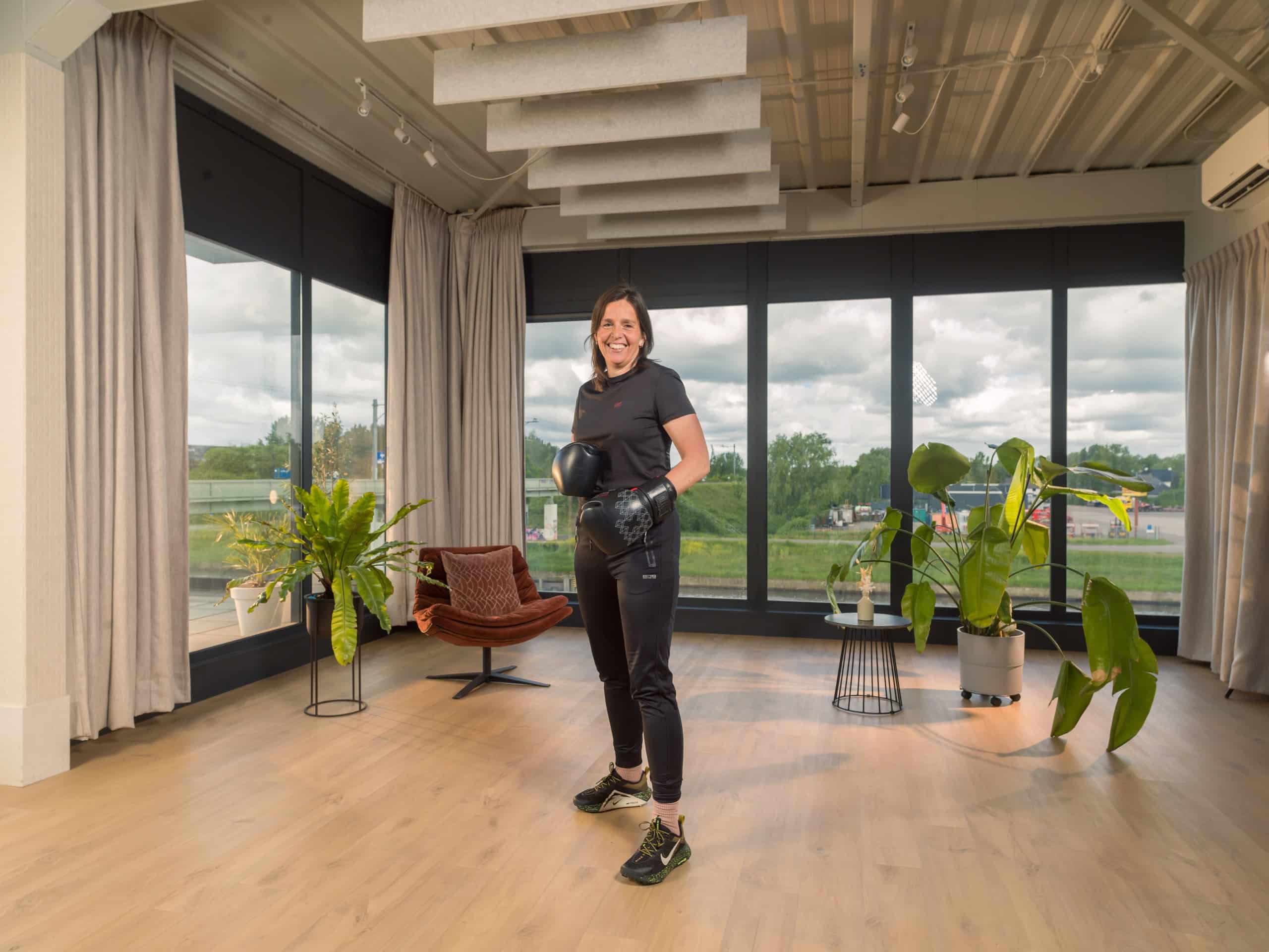 Vrouw met bokshandschoenen staat in een lichte trainingsruimte met planten