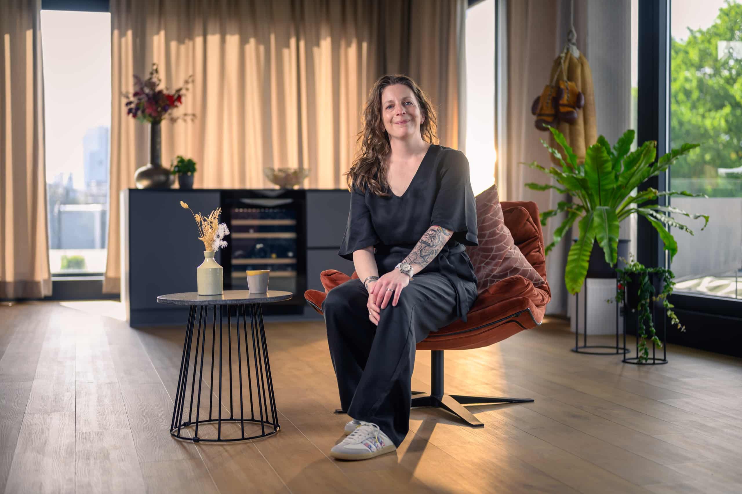 Vrouw zit ontspannen en glimlachend in een fauteuil in een lichte ruimte