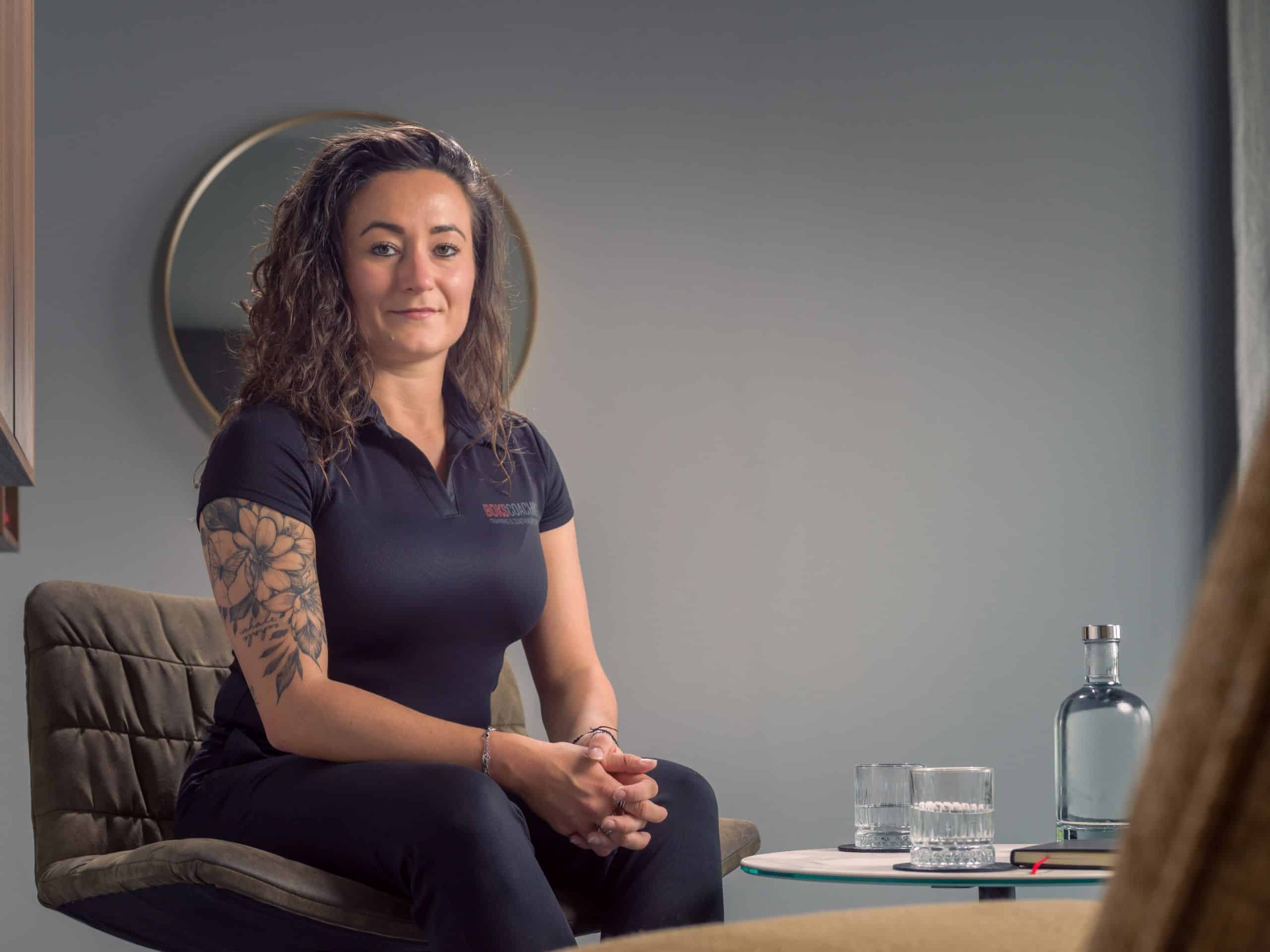 Coach zit glimlachend in een fauteuil in een coachruimte