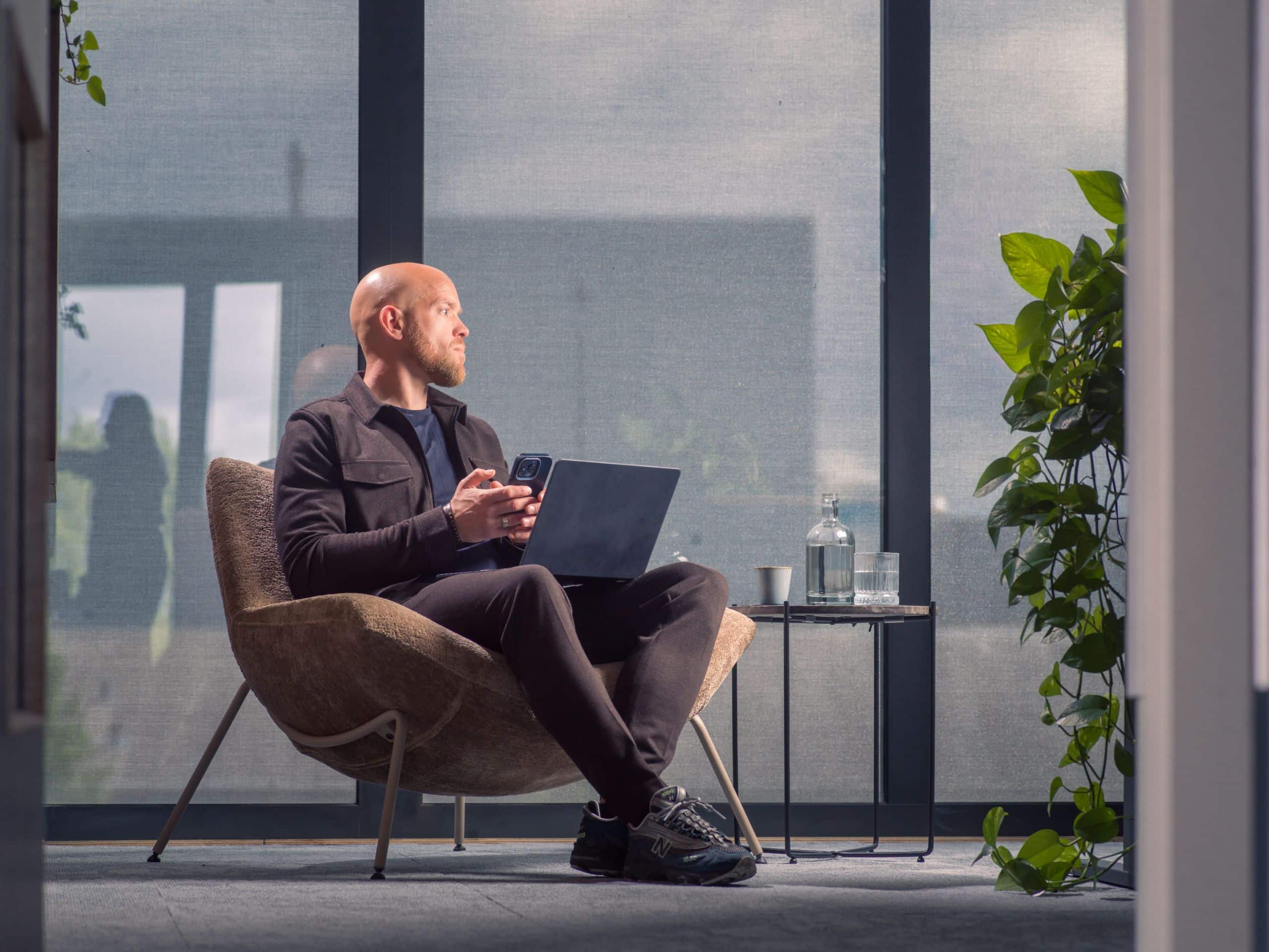 Manager zit met laptop in een fauteuil bij een groot raam