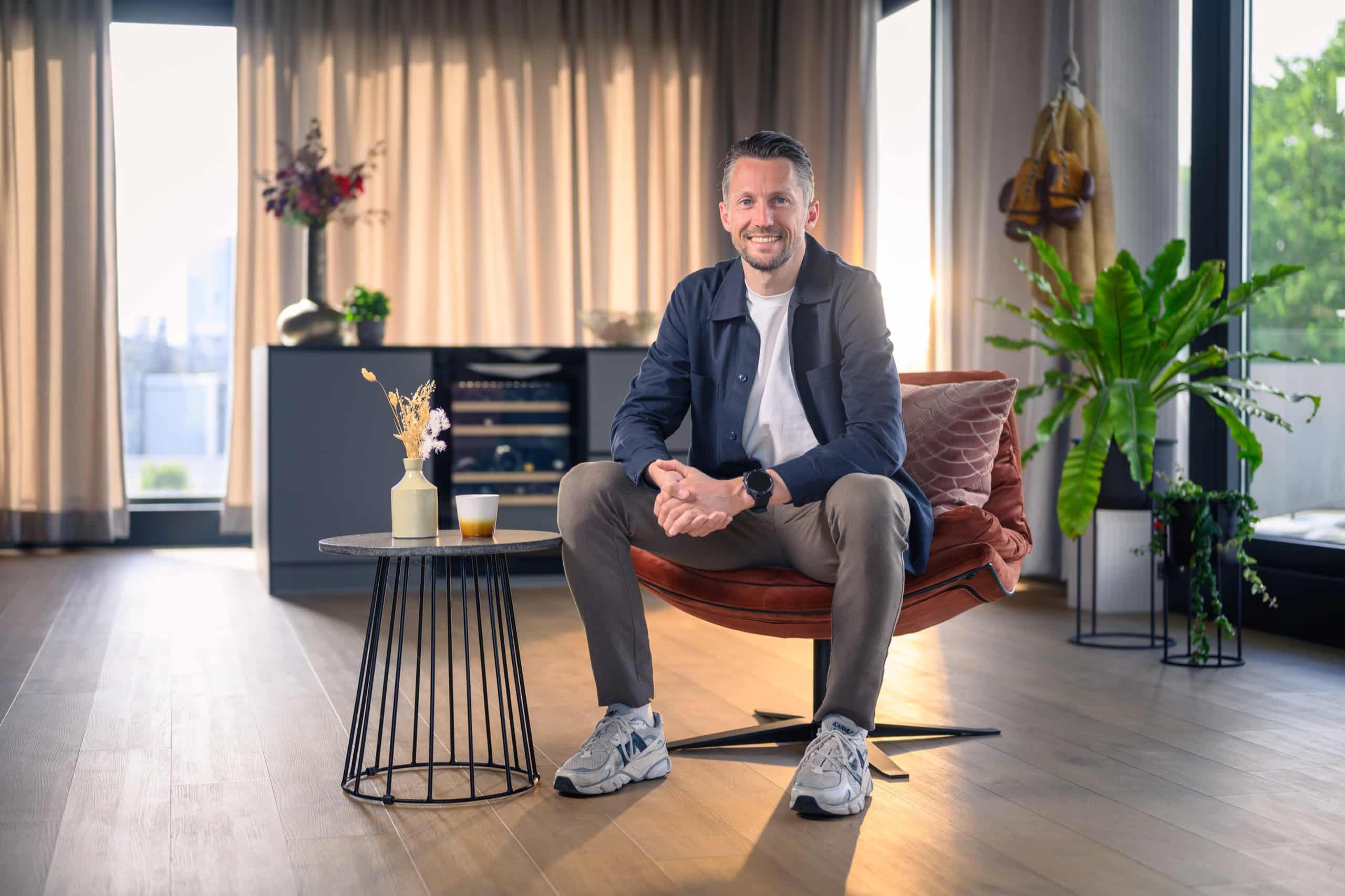Man in blazer zit zelfverzekerd in een fauteuil in een lichte ruimte