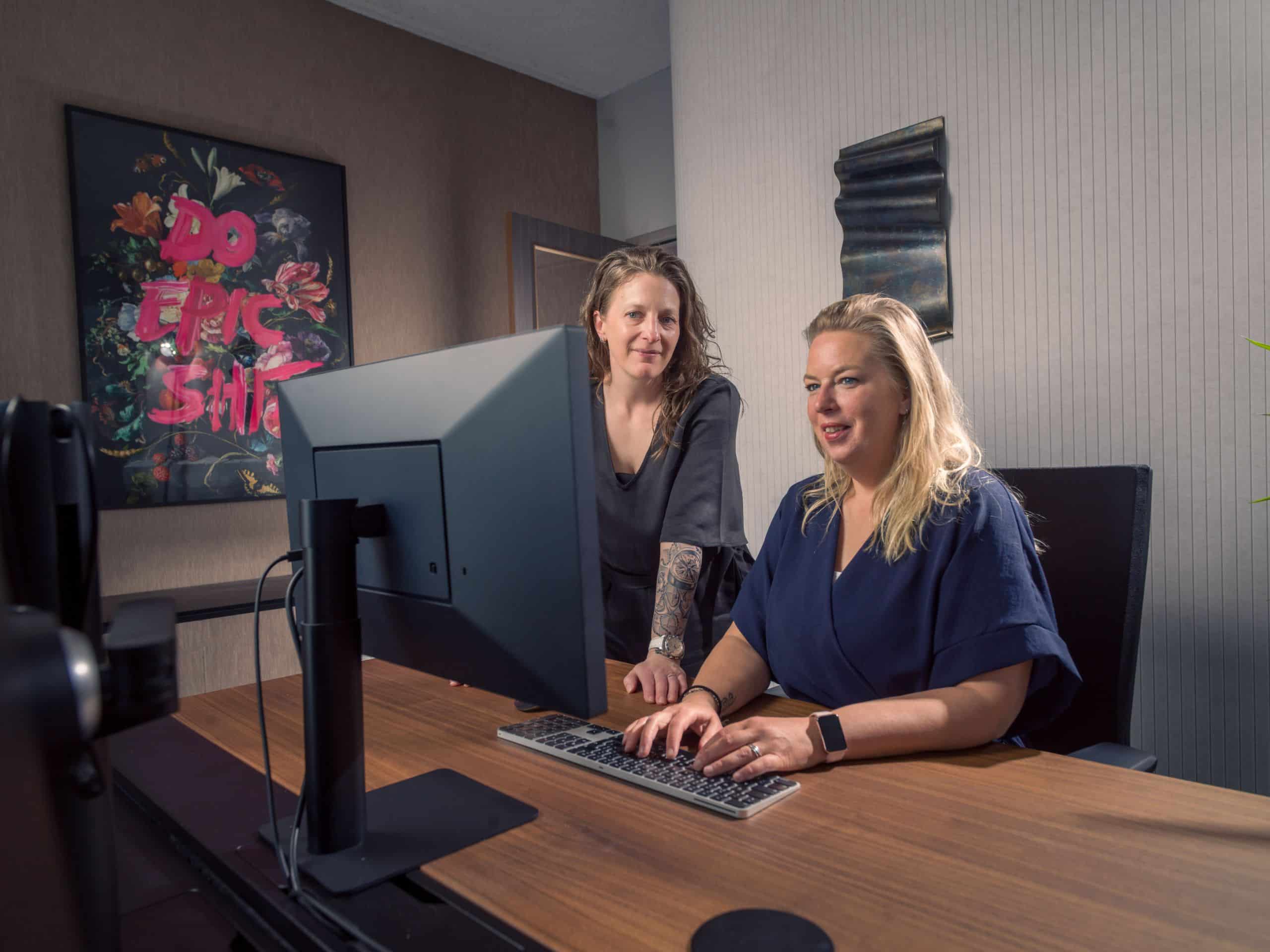 Twee mensen werken samen achter een computer aan een bureau