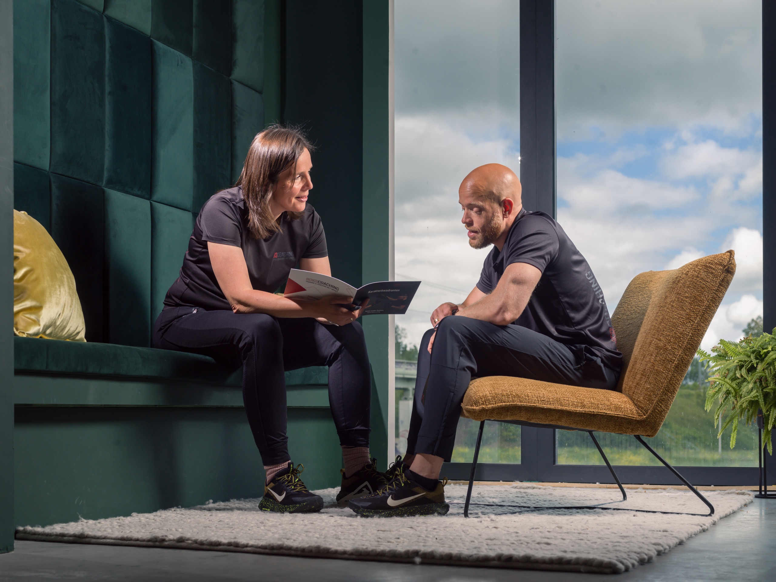 Twee mensen in gesprek op een groene bank bij het raam